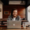 man in black and white striped polo shirt sitting on chair in front of silver macbook