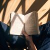 person holding book sitting on brown surface